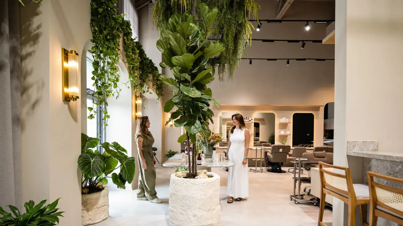 Luxury biophilic hair salon in Miami with lush greenery, arched doorways, and warm lighting, designed by Paula Ambrosio Interiors