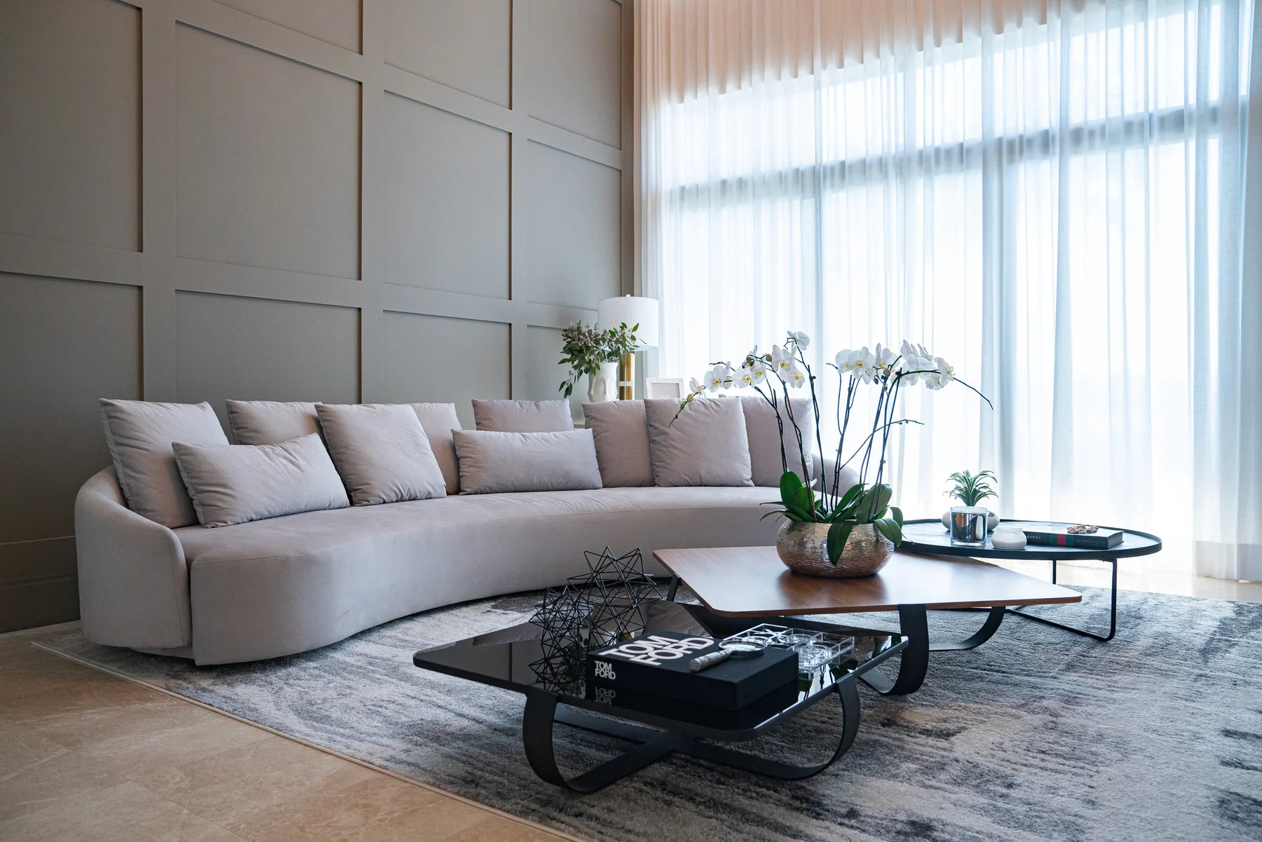 Living room with a curved grey sofa, marble wall panels and soft daylight