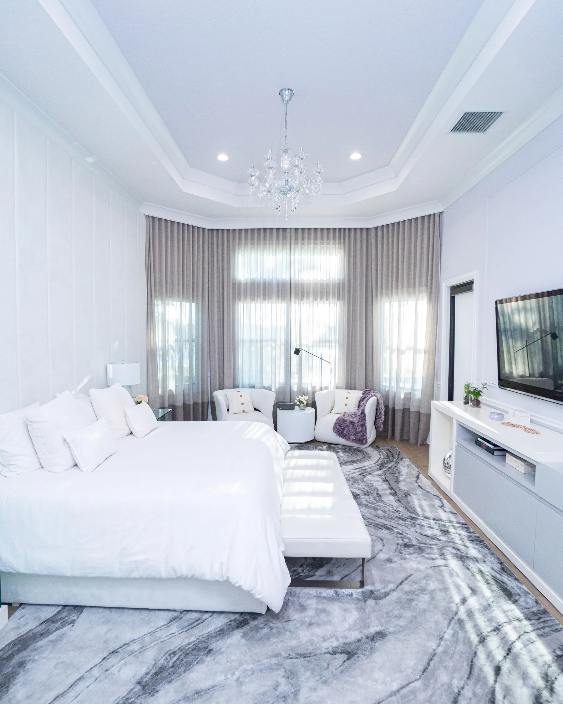 Bedroom with a statement chandelier, upholstered headboard and a wall-mounted television