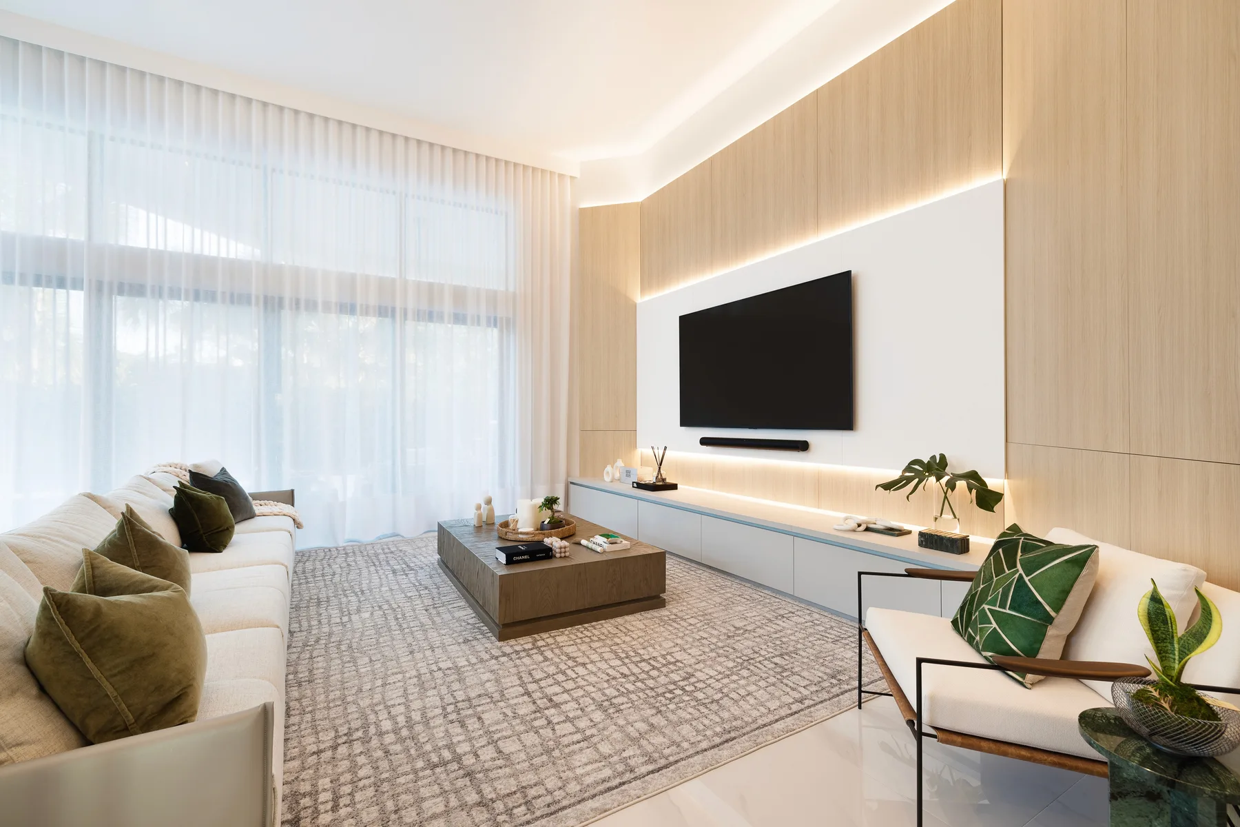 Living room with a grey sectional, media wall and floor-to-ceiling sheer curtains