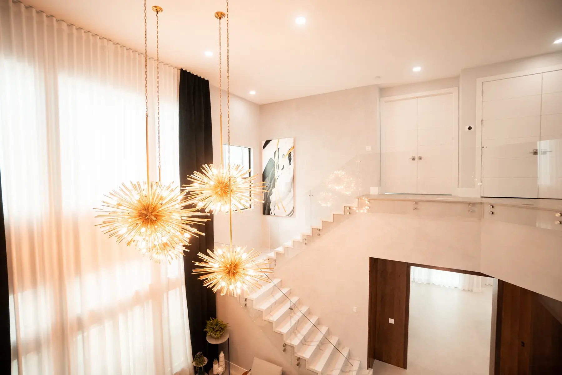 Luxury double-height foyer with gold starburst chandeliers and marble staircase in HOME TR residence by Paula Ambrosio Interiors