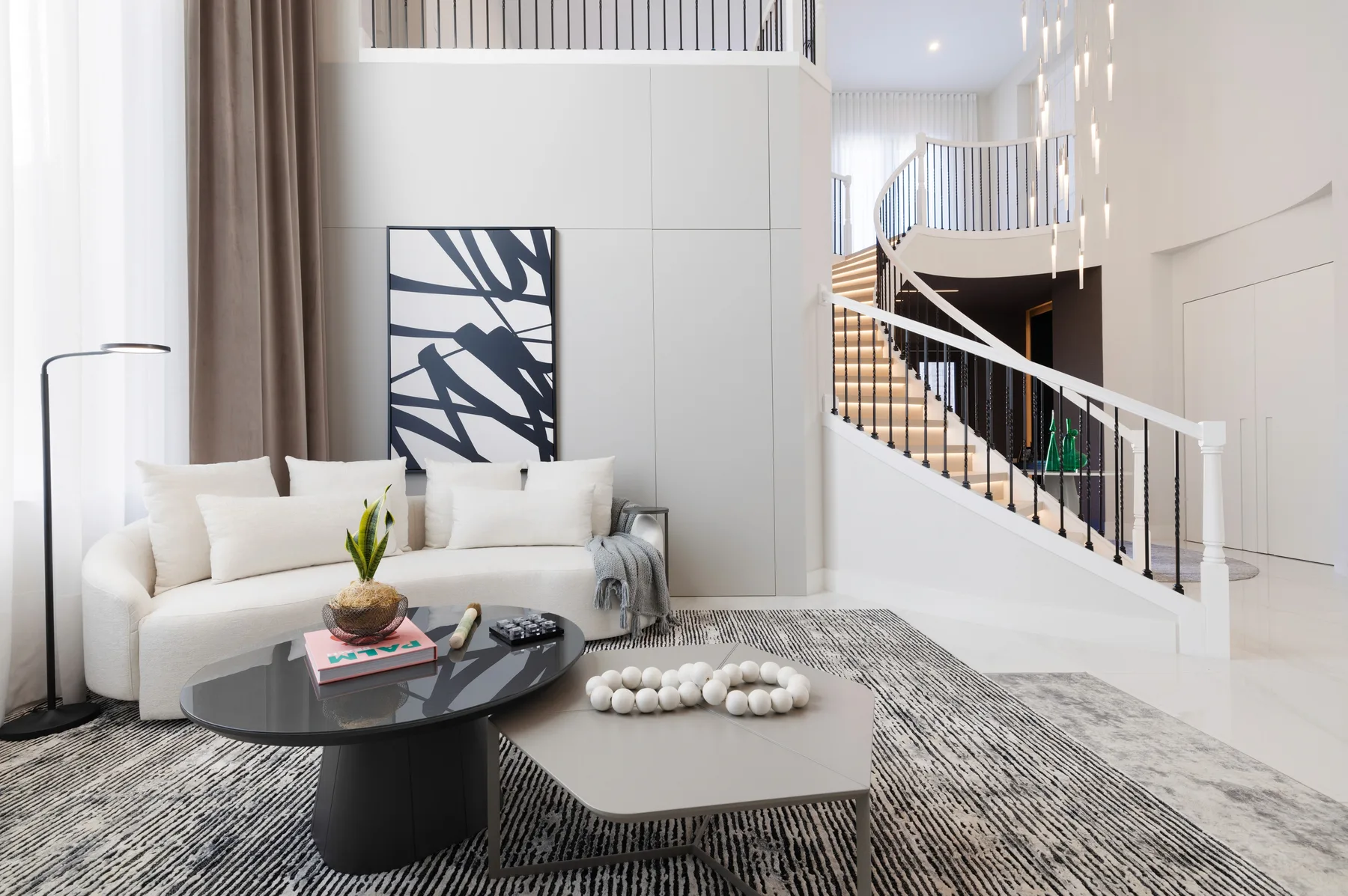 Bright living room with white sofas, sculptural artwork and an open staircase