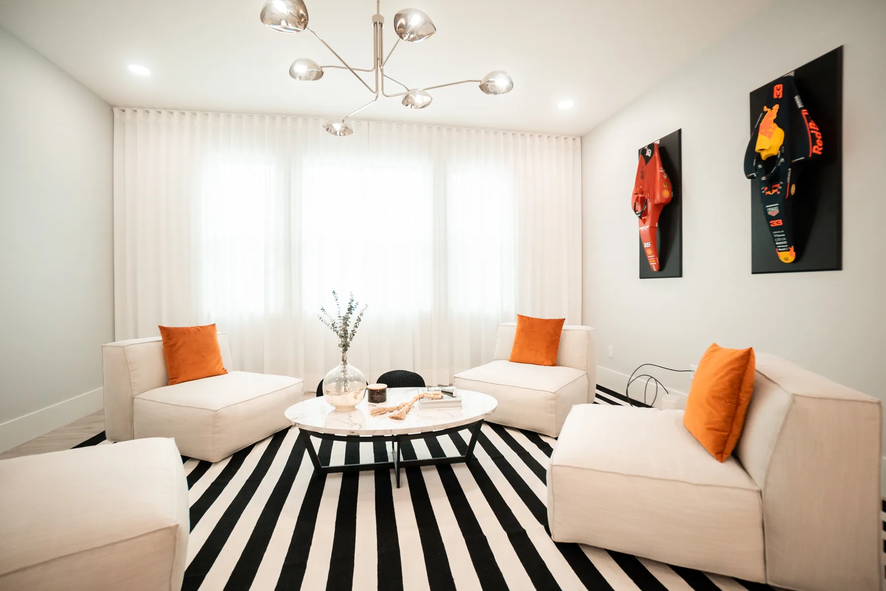 White living room with a black-and-white striped ottoman and coral accent pillows