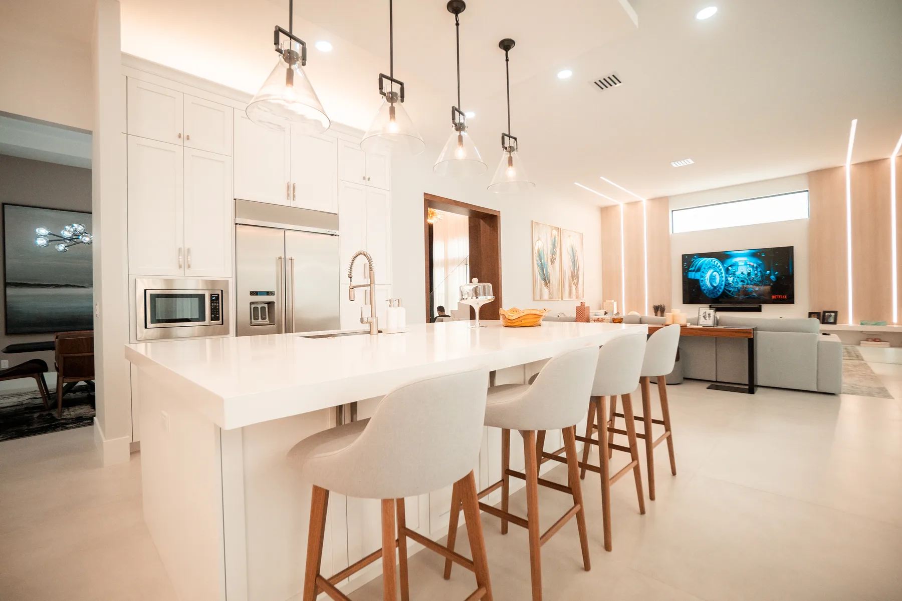 White kitchen with a waterfall island, pendant lighting and leather bar stools