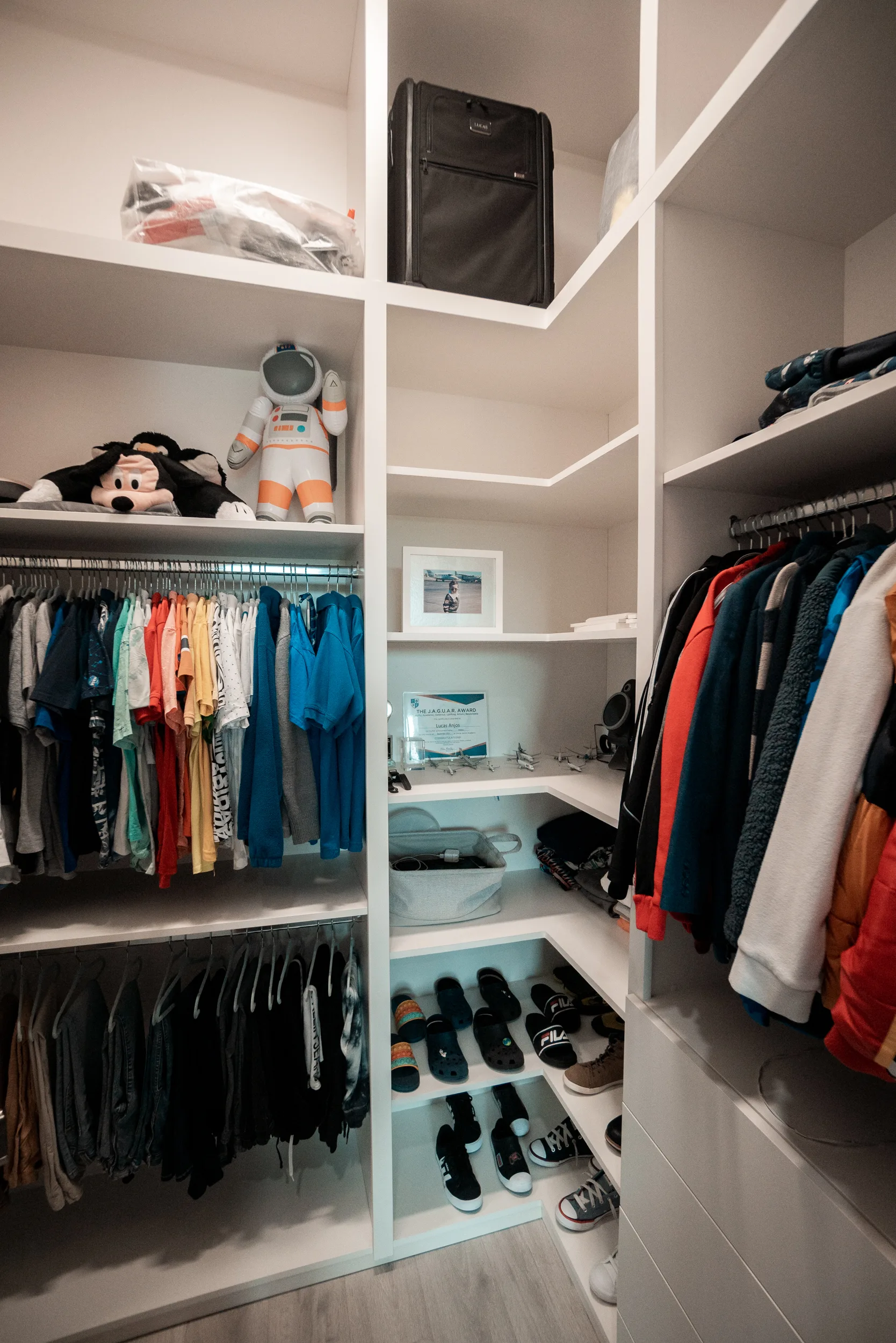 Children's walk-in closet with colorful open hanging rods, toy display and bright storage bins